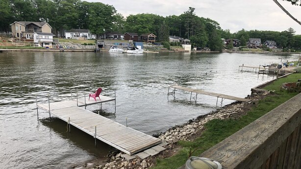 A waterfront property with a dock, a red chair, and a small boat. - Dock Life Cottage 4 - Riverside, 1 Bedroom, Wasaga (Wasaga Beach)