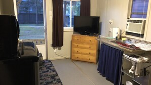 A compact kitchen with a television, wooden dresser, and a window with curtains. - Dock Life Cottage 4 - Riverside, 1 Bedroom, Wasaga (Wasaga Beach)