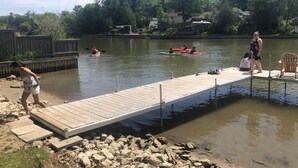 A wooden dock extending into a calm body of water, surrounded by rocks and greenery. - Dock Life Cottage 4 - Riverside, 1 Bedroom, Wasaga (Wasaga Beach)