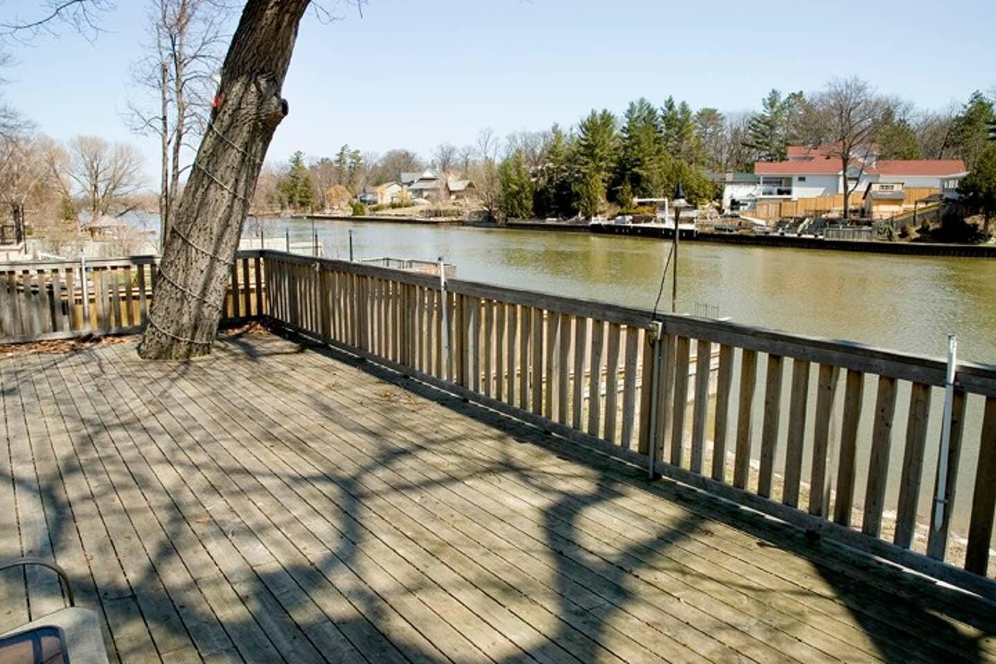 Een houten terras met een balustrade, met uitzicht op een rivier, omringd door bomen en woongebouwen.
