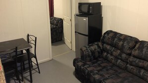 A compact room with a kitchenette, a sofa, a dining table with chairs, and a door leading to another room. - Dock Life Cottage 4 - Riverside, 1 Bedroom, Wasaga (Wasaga Beach)
