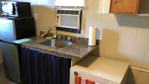 A compact kitchen with a sink, a microwave, a refrigerator, and a small cabinet.