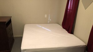 A small, unadorned room with a single bed, a dresser, and a power outlet on the wall.