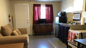 A compact living space with a kitchenette, a sofa, a small table, and a television.
