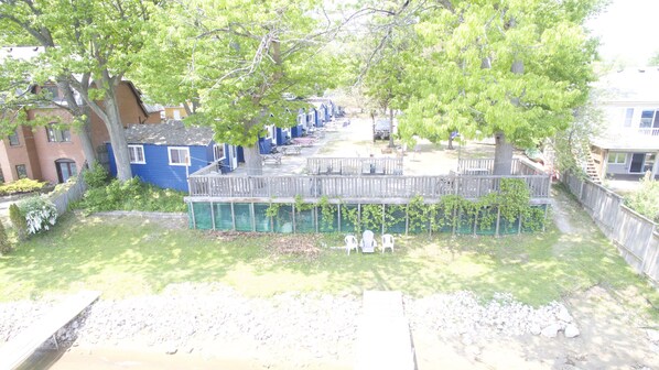 A residential area with a wooden deck, a swimming pool, and houses with blue siding. - Dock Life Cottage 8 - Riverside, 1 Bedroom, Wasaga (Wasaga Beach)