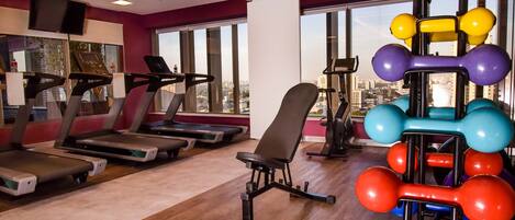 A gym with treadmills, a weight bench, and colorful dumbbells.