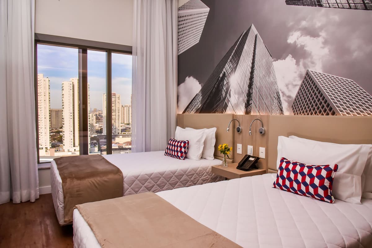 A hotel room with two beds, a city view, a modern wall art, and a nightstand with a phone.