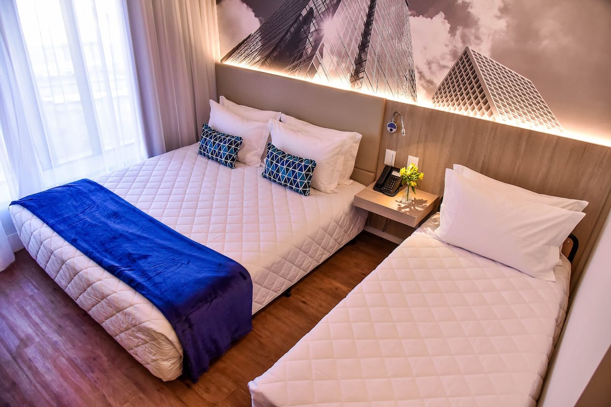 A hotel room with two beds, a nightstand, and a wall-mounted lamp.
