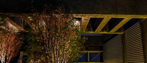 Un espace extérieur aménagé avec des jardinières et un élément décoratif aquatique, situé sous une structure couverte et offrant une vue sur la façade du bâtiment.