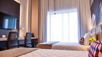 Een hotelkamer met twee bedden, een bureau, een stoel, een televisie en een groot raam met gordijnen.