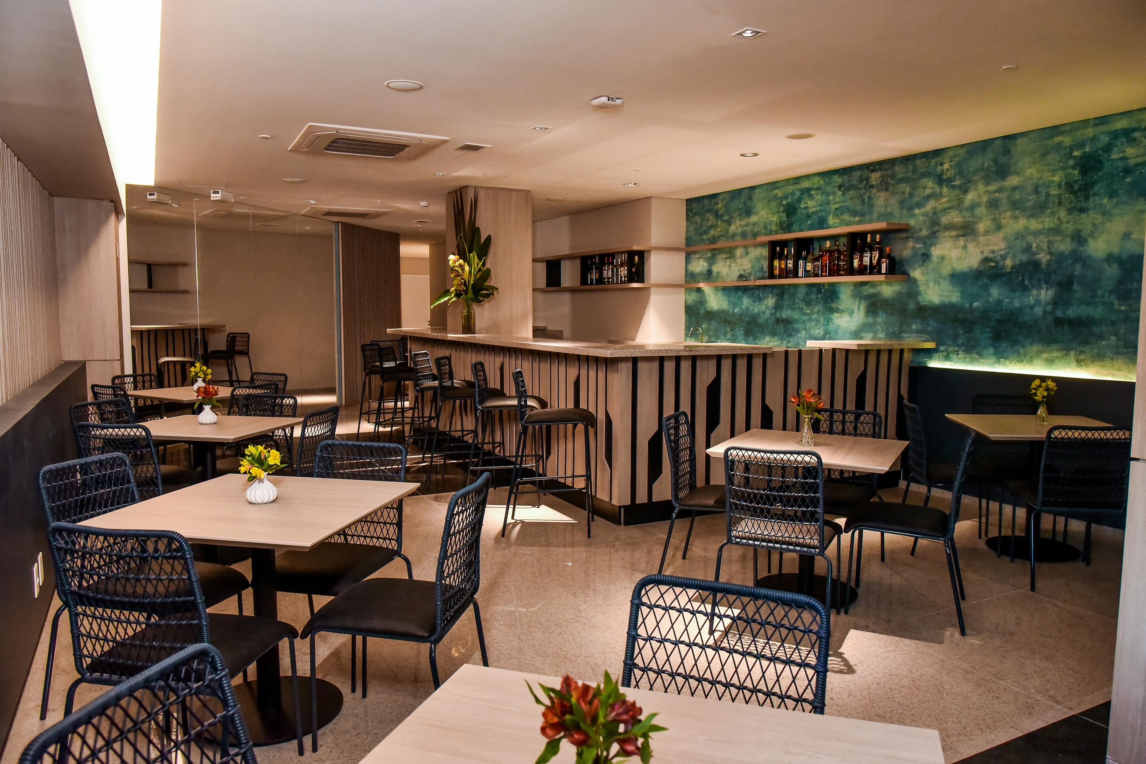 Un restaurante moderno con una zona de bar, mesas de madera y sillas negras.