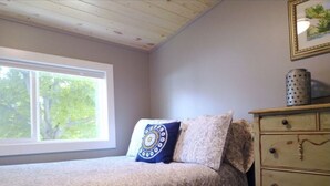 A bedroom with a bed, a dresser, and a window with a view of trees.
