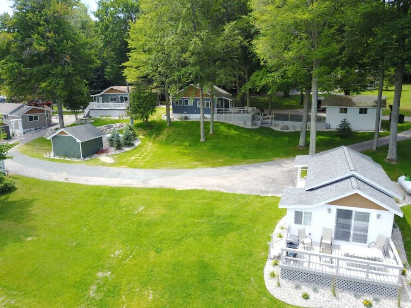 A residential area with multiple houses, a well-maintained lawn, and a driveway leading to a house with a deck and outdoor seating.