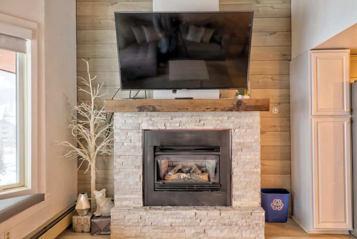 A modern living room with a stone fireplace, a flat-screen TV mounted above it, and a window on the left.