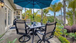 An outdoor patio with a table and chairs, a large umbrella, and a barbecue grill. - Two Homes, One
 Lot Sleeps 18, Pool & Hot Tub Private Villa, 9 miles from beach. (Vista)