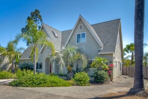 A two-story house with a sloped roof, a front porch, and a well-maintained garden with various plants and a palm tree.
