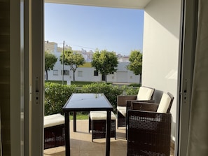 Een balkon met rieten meubels en een tafel, uitkijkend op een woonwijk met huizen en bomen.