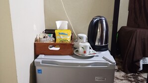 Un refrigerador compacto con una etiqueta de eficiencia energética BLACKPOINT, una cafetera, una taza, una caja de totopos Original St. Maries y una caja de pañuelos.