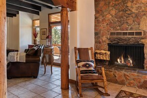 A cozy living room with a stone fireplace, a leather sofa, a rocking chair, and a dining area with a table and chairs. - Sunlit Pines - Tucked in the Trees, Private Escape, Easy Drive to Plaza - NEW Listing (Santa Fe)