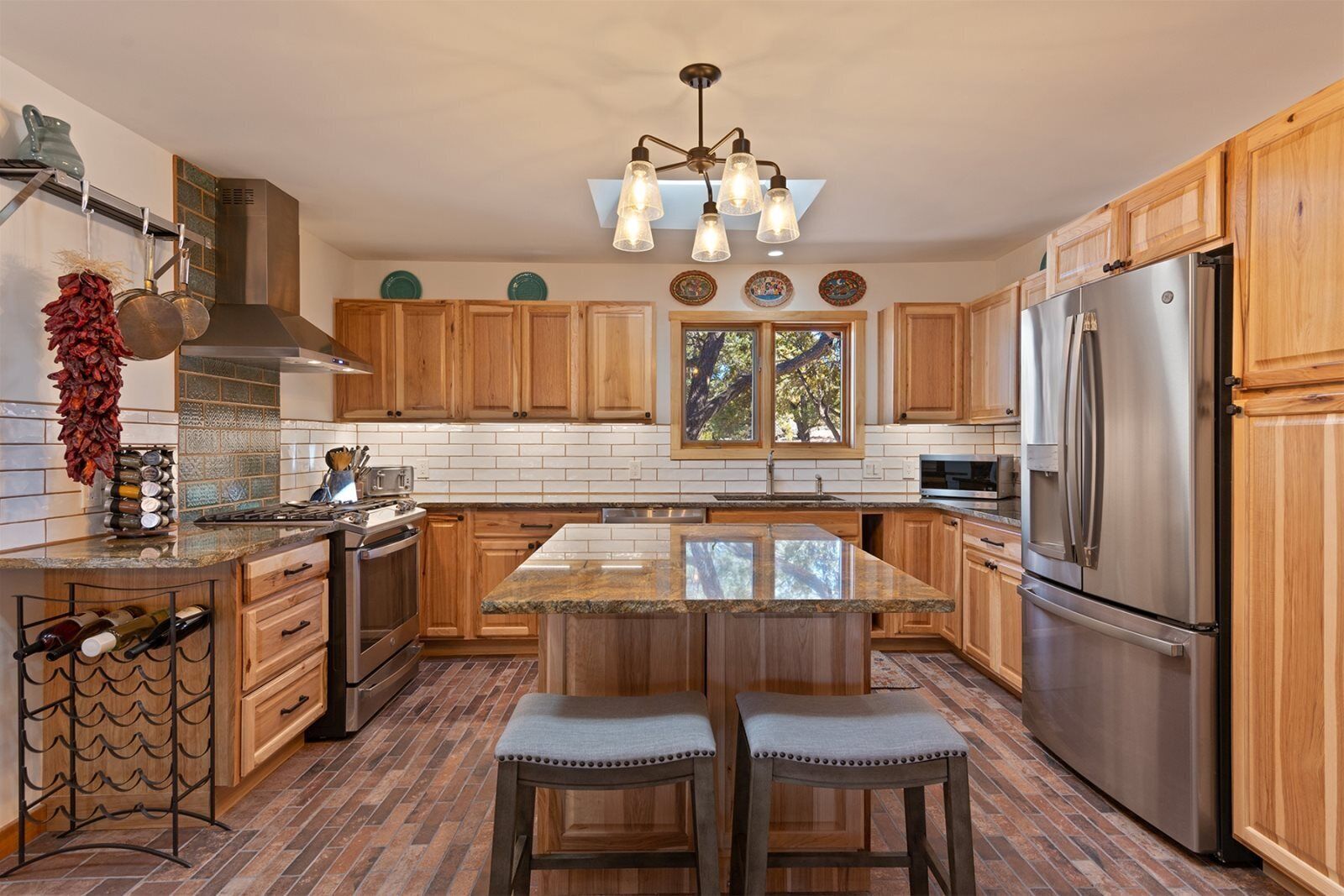 A kitchen with wooden cabinets, a stainless steel refrigerator, a central island with stools, and a hanging light fixture.