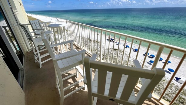 A balcony with white chairs and a table overlooking a beach with umbrellas. - Directly on the Ocean! Beautiful Views! Free Beach Chairs and Umbrella sleeps 6 (Pensacola Beach)