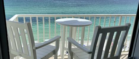 Un balcon avec deux chaises blanches et une petite table ronde, donnant sur un océan turquoise sous un ciel dégagé.