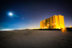 A beachfront hotel with multiple floors and balconies, a sandy beach in the foreground, and a starry night sky.