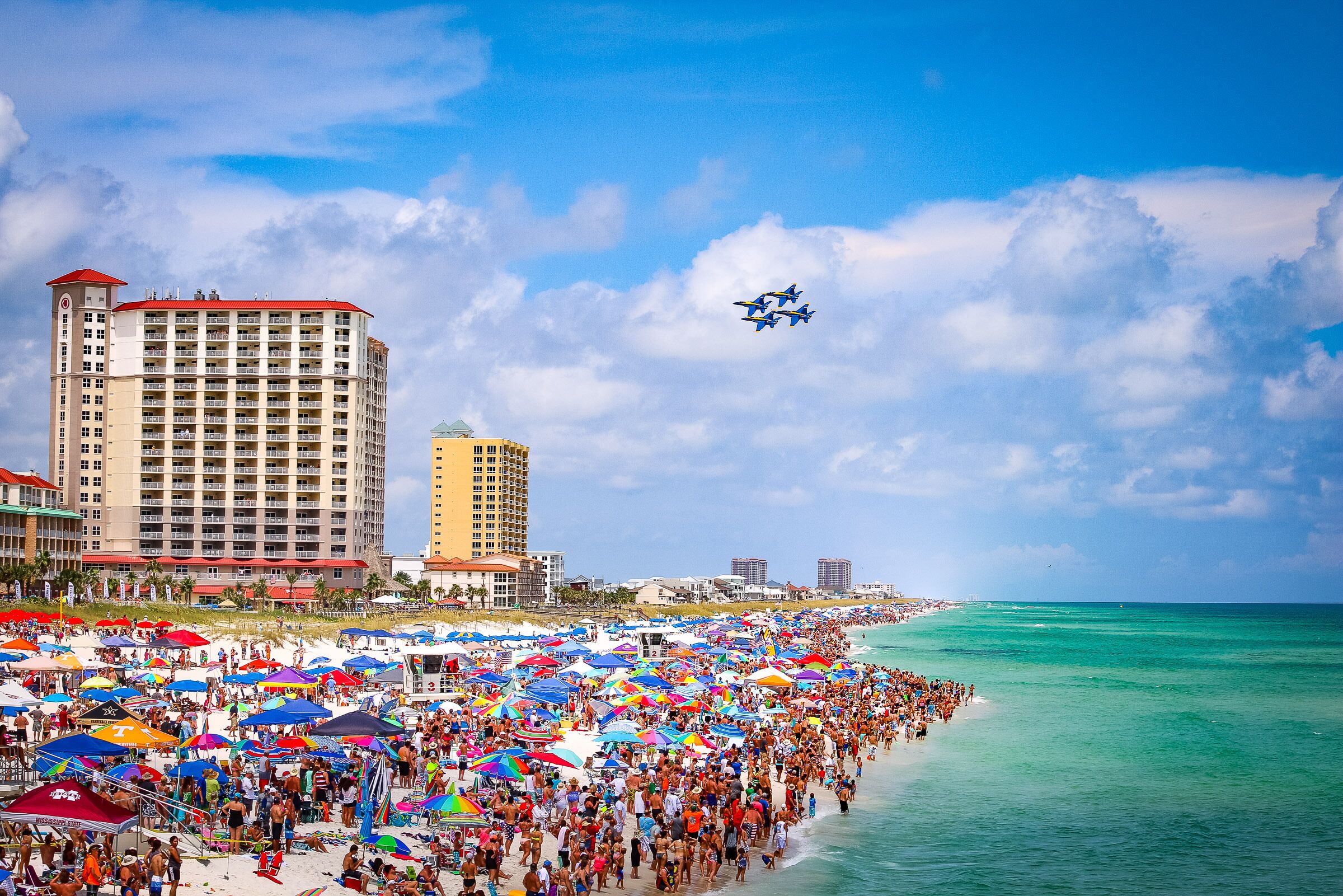 A crowded beach with numerous umbrellas and people.