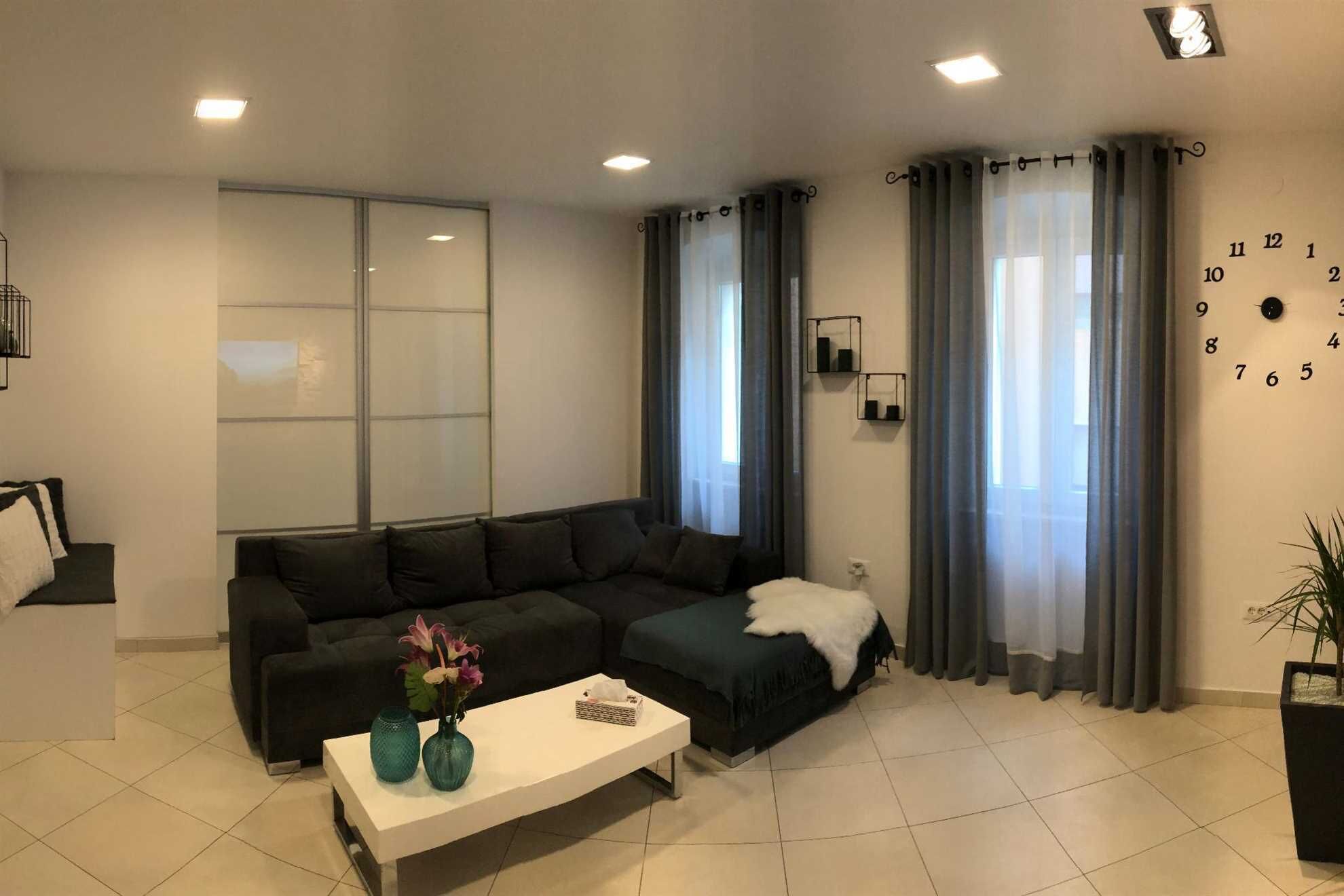Ein modernes Wohnzimmer mit einem Ecksofa, einem weißen Couchtisch und einem großen Fenster mit Vorhängen.