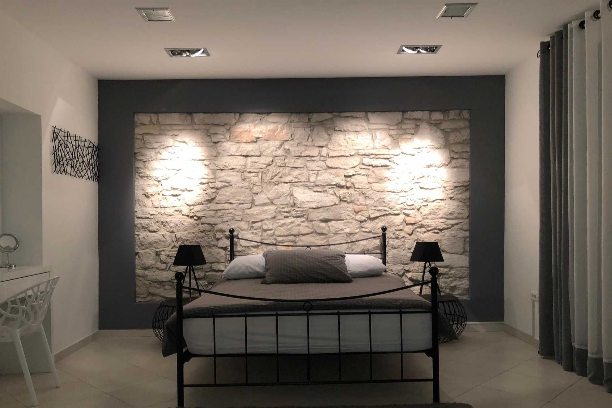 Una camera da letto con parete in pietra, un letto con due lampade nere e una sedia.