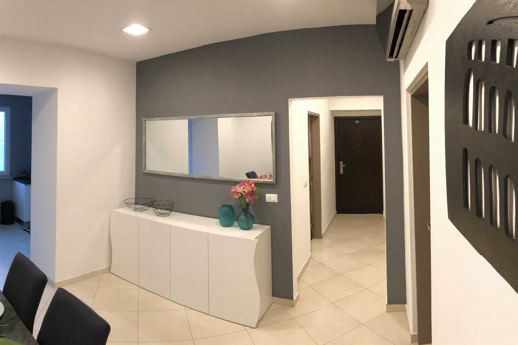 A modern hotel lobby with a curved white reception desk, a large mirror, and a vase with flowers.