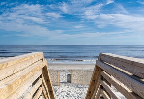 A wooden beach walkway leading to the ocean with a clear sky.