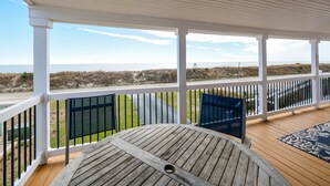 Ein überdachter Außenbereich mit Holzterrasse, zwei Stühlen und Blick auf den Strand.