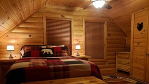 A cozy log cabin bedroom with a bed, two bedside lamps, a wooden bench, and a decorative rug.