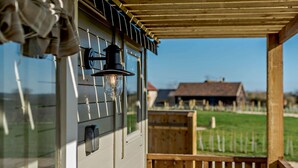 A wooden deck with a railing, a clear sky, and a distant view of a house and fields. - Luxury shepherd's hut for 2 in the Cotswolds - Aurora (Faringdon)
