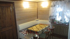 A cozy cabin interior with a wooden wall, a bench, a table with a quilt, and a window with curtains. - Cozy guest house near Braslaw lakes (Braslaw)