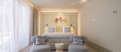 A modern bedroom with a bed, two armchairs, a round side table, and a large window with sheer curtains.