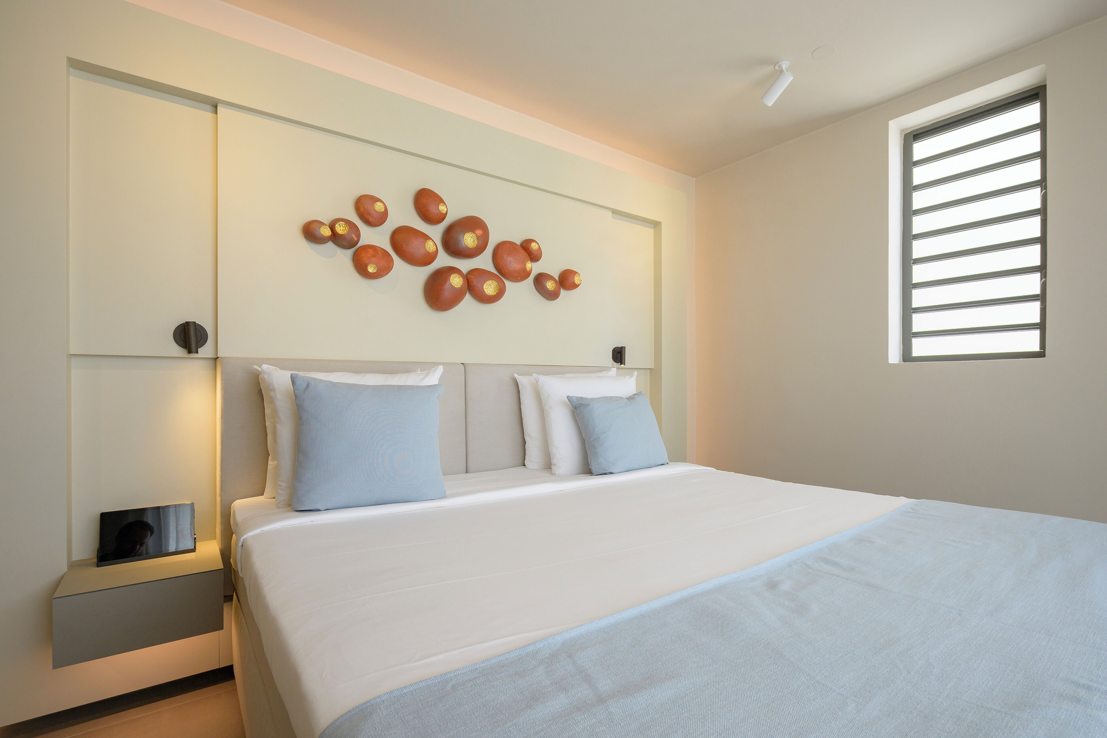 Una habitación de hotel moderna con una cama grande, una mesita de noche con lámpara y una lámpara de pared.