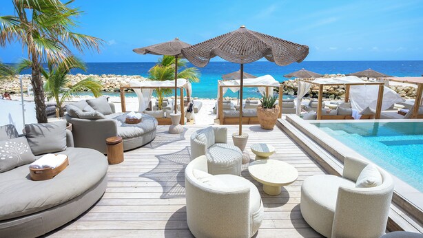 Eine Holzterrasse mit Sitzgelegenheiten im Freien, einem Pool und Blick aufs Meer.