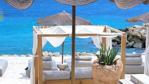 Eine Strandlounge mit Holzterrasse, weißen Sitzkissen und einer großen Topfpflanze.