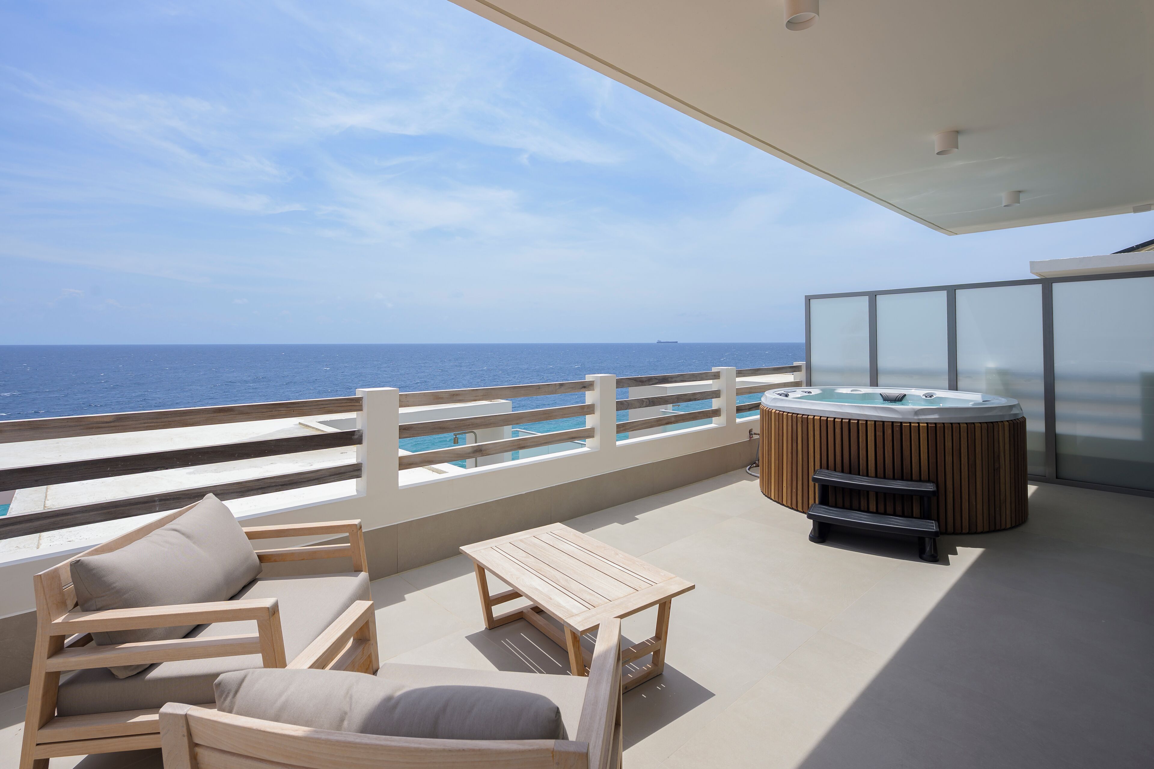 Ein Balkon mit Holzmöbeln, einem Whirlpool und Blick aufs Meer.