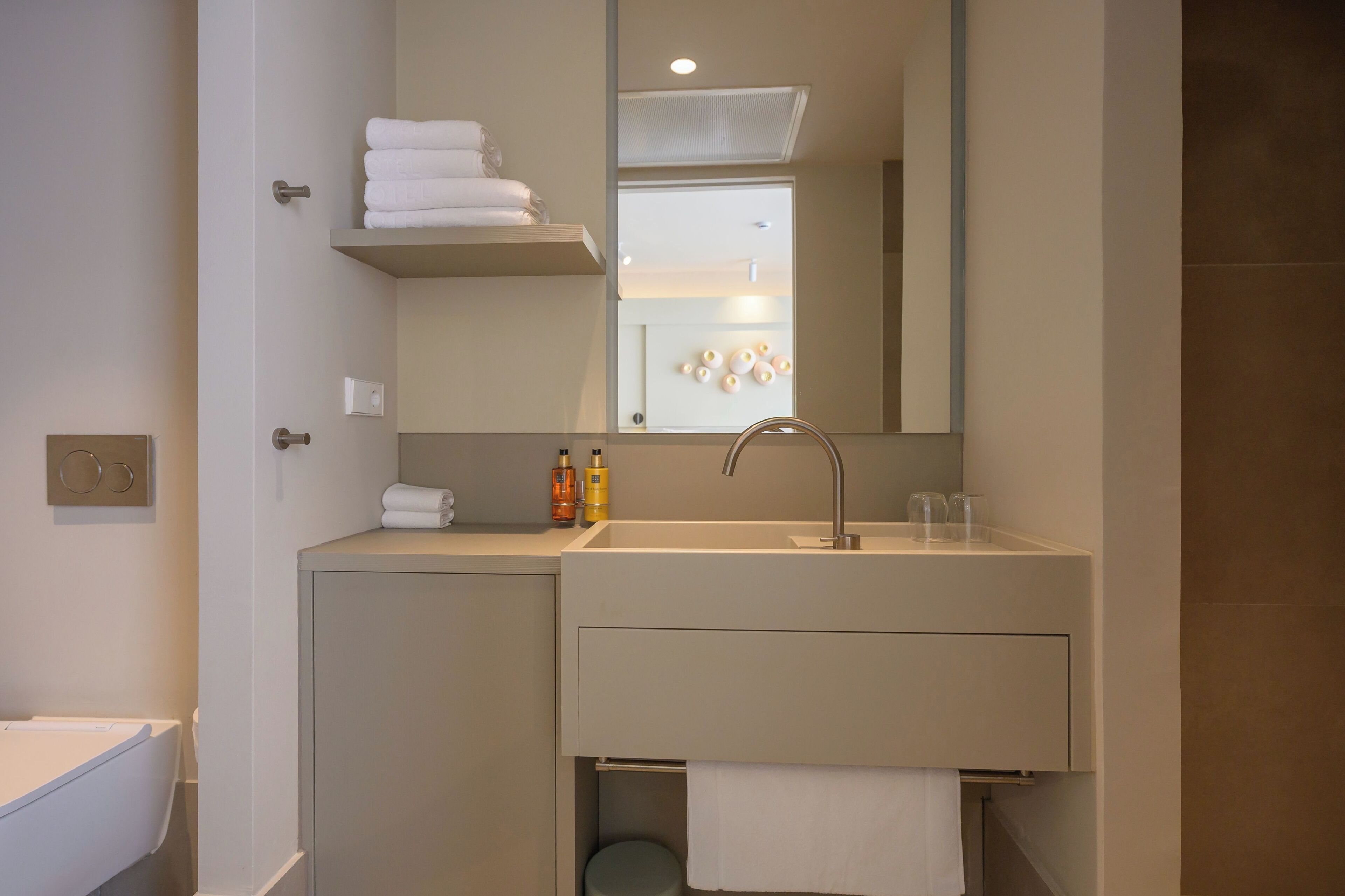 Een moderne badkamer met een grote spiegel, een wastafel en een toilet. Op het aanrecht liggen handdoeken en toiletartikelen.
