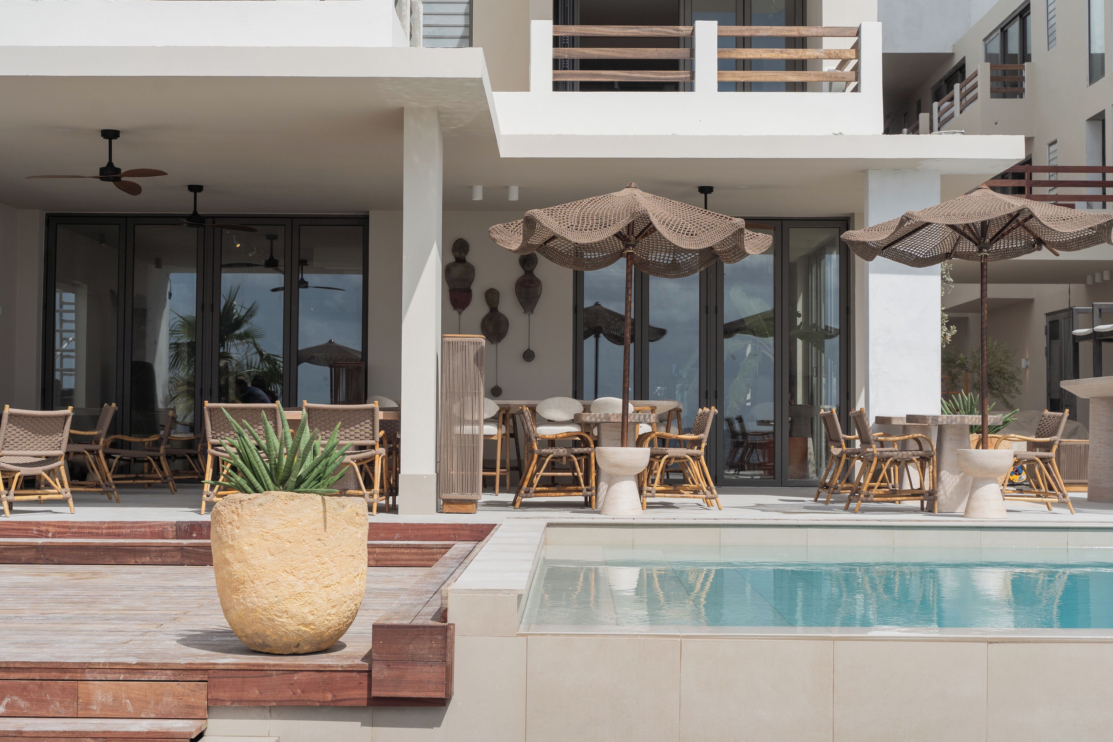Zona de piscina con mobiliario exterior y sombrillas, rodeada por un edificio moderno con balcones.