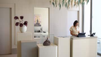 A modern reception desk with a receptionist, a vase with dried flowers, and a sculpture on display.