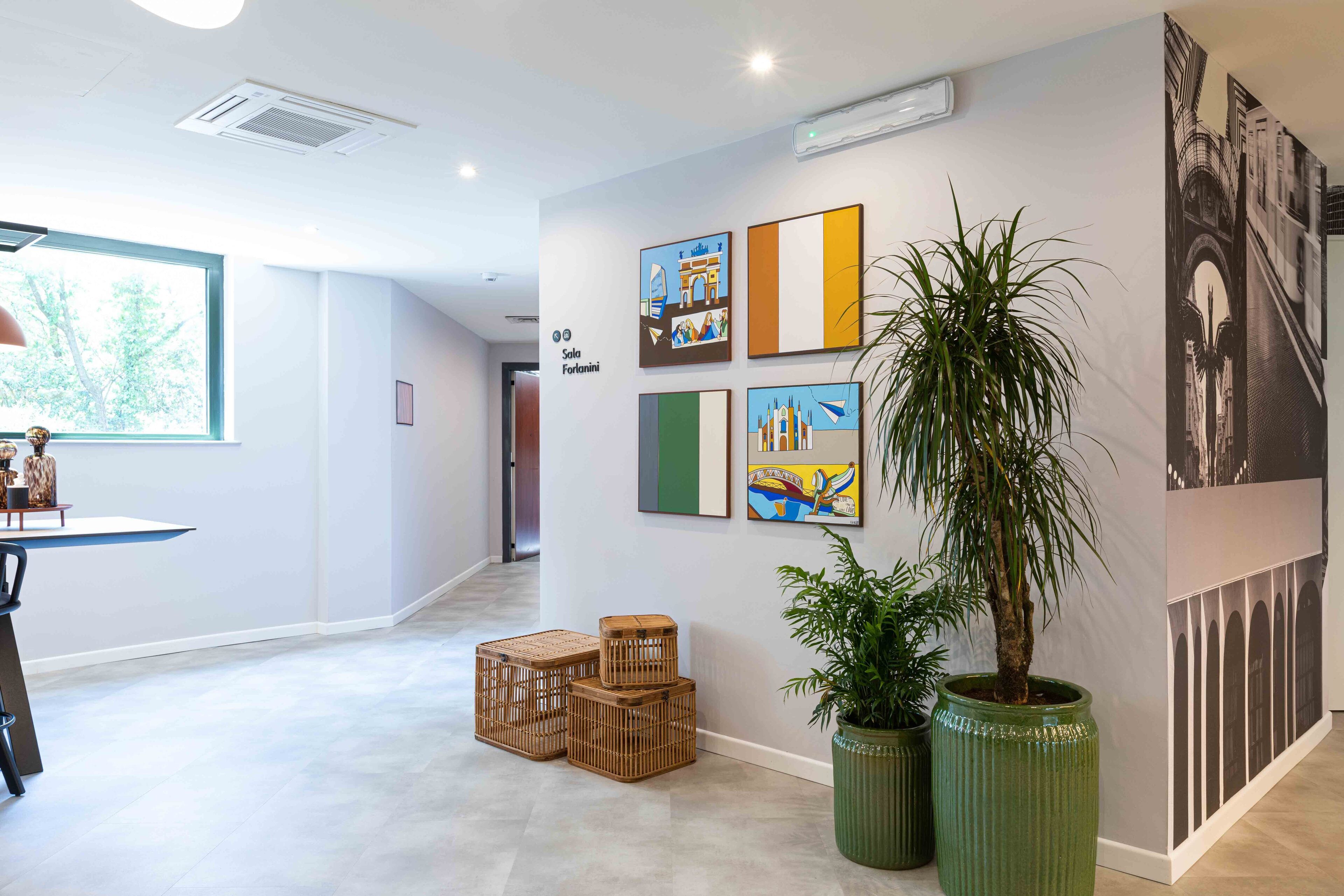 Una hall d'albergo moderna con una reception, un'ampia finestra e opere d'arte alle pareti.