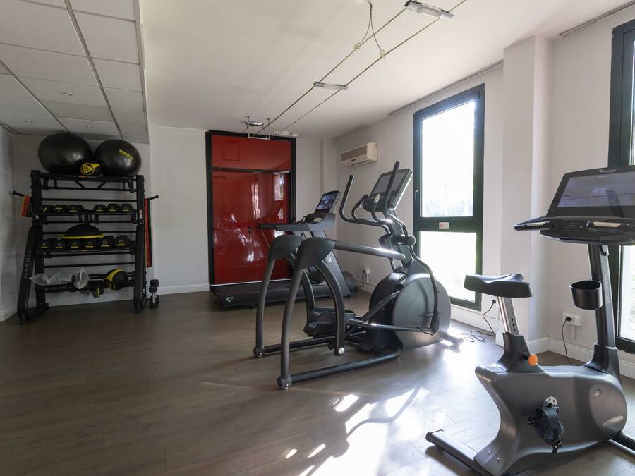 Un gimnasio con equipamiento de ejercicio, cinta de correr y bicicleta estática.