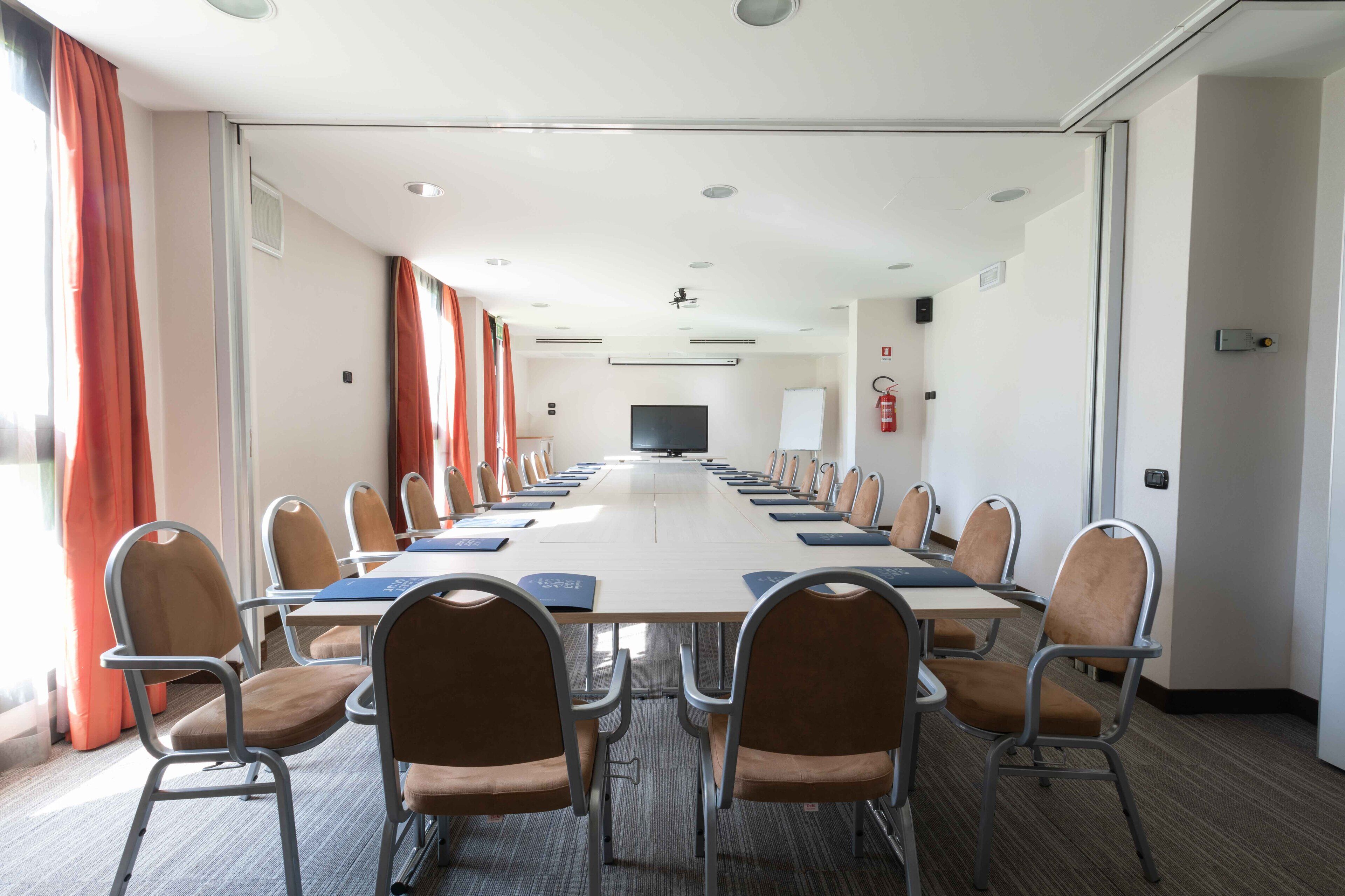 Una sala conferenze con un lungo tavolo, sedie, uno schermo per proiettore e una lavagna.
