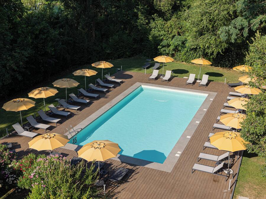 A rectangular swimming pool surrounded by lounge chairs and yellow umbrellas on a wooden deck.