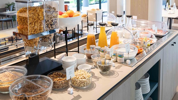 Een ontbijtbuffet met diverse soorten eten en drinken, zoals cornflakes, fruit en vruchtensappen.