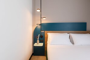 Una habitación de hotel moderna con una cama bien hecha, una mesita de noche con un jarrón de flores y una lámpara fijada a la pared.